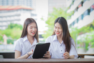 Two young Asian girls students are consulting together and using a tablet to search information for a study report.