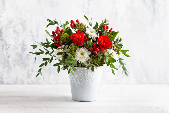 Festive winter flower arrangement with red roses, white chrysanthemum and berries in vase on table. Christmas flower composition for holiday.