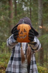 child in halloween costume holding a decorative lantern pumpkin in front of his face