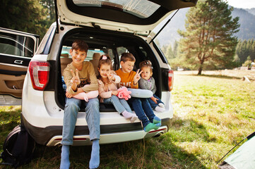 Family of four kids at vehicle interior. Children sitting in trunk. Traveling by car in the mountains, atmosphere concept.