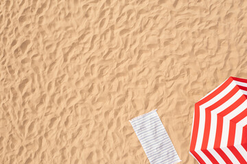 Striped beach umbrella near towel on sand, aerial view. Space for text