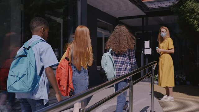 Woman Is Measuring Temperature Of Kids At The Entrance In School, Covid Restrictions. Children Are Safely Going To School In Pandemic. High Quality 4k Footage