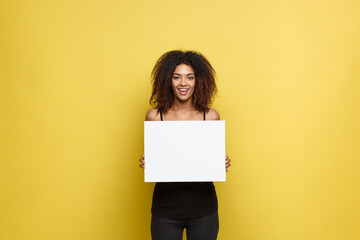 Obraz na płótnie Canvas Business Concept - Close up Portrait young beautiful attractive African American smiling showing plain white blank sign. Yellow Pastel studio Background. Copy space