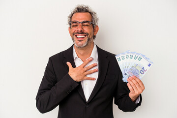 Middle age business man holding bills isolated on blue background  laughs out loudly keeping hand on chest.