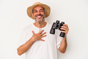 Fototapeta na wymiar Middle age caucasian man holding binoculars isolated on white background laughs out loudly keeping hand on chest.