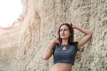 slim sporty girl in a casual clothes posing against the rocks of sand in quarry