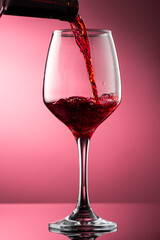 pouring red wine into glass with highlights on red background