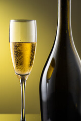 tall champagne glass next to bottle with highlights on yellow background