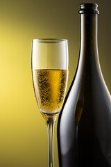 tall champagne glass next to bottle with highlights on yellow background