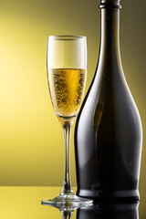 tall champagne glass next to bottle with highlights on yellow background