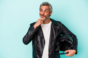Middle age biker caucasian man holding helmet isolated on blue background  looking sideways with...