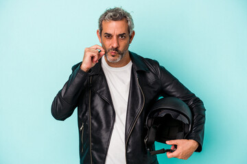 Middle age biker caucasian man holding helmet isolated on blue background  with fingers on lips...