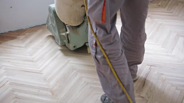 Repairman restoring parquet with a sanding machine.