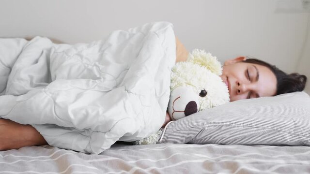 Young woman goes to sleep with teddy bear in her bedroom. Phone addiction, insomnia. Checking social media. Circadian rhuthm.