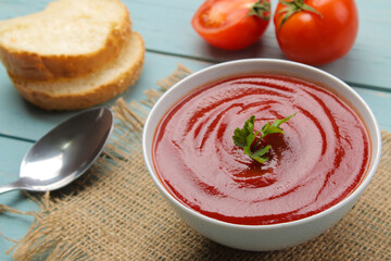 Tomato soup with herbs with bread in a white bowl with a spoon on a blue wooden table. Tasty food.