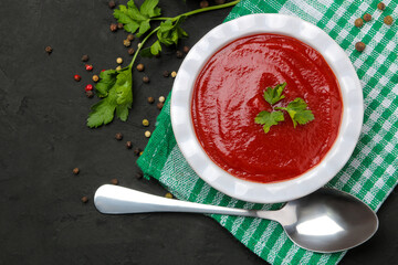 Delicious tomato soup on a black table, parsley and spices on a black table. top view.