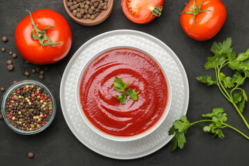 Delicious tomato soup on a black table and ingredients for cooking tomatoes and spices