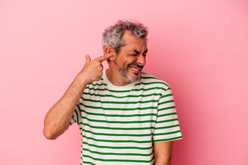 Middle age caucasian man isolated on pink background  covering ears with hands.