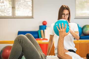 Man patient and female physiotherapist exercising with a small pilates ball with both hands, in...