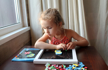 The girl collects a figure from multicolored and different-shaped parts, a mosaic. Exercises for fine motor skills, the development of attention, accuracy, speech and other skills. 
