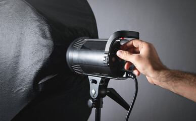 Male hand adjusts flash in studio.