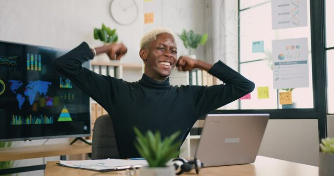 Good-looking smiling satisfied successful young african american guy overjoyed from good news on laptop screen when working in office room,front view