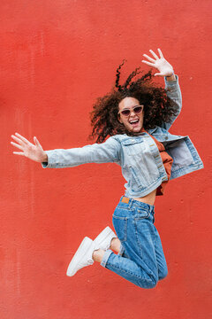 Happy woman wearing sunglasses jumping in front of red wall