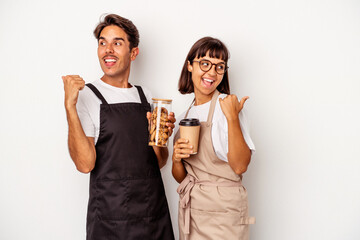 Young mixed race store clerk couple isolated on white background points with thumb finger away, laughing and carefree.