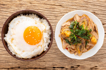streamed rice with fried egg, sesame on top beside basil stir fried century egg, sliced pork and crispy basil leaves on top on natural wood texture background, Pad Ka Prao Kai Yeow Ma, Thai food
