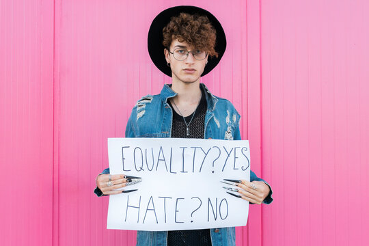 Serious gay man holding placard in front of pink wall
