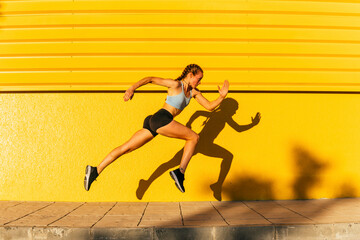 Young female athlete exercising while running by yellow wall