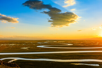 Bayinbuluke Grassland and winding river natural scenery in Xinjiang at sunset,China.The winding river is on the green grassland.