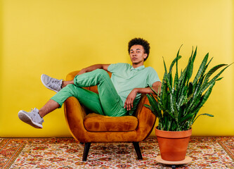 Young man sitting on armchair by plant