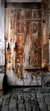 Shuttered leaning wooden door with weathered peeling brown glaze on a floor of cobblestones