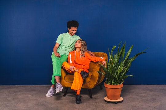 Friends looking at each other while sitting on armchair at studio - Powered by Adobe