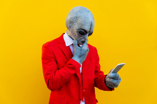 Portrait of man wearing alien costume and bright red suit using smart phone