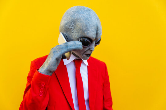 Portrait of man wearing alien costume and bright red suit using smart phone