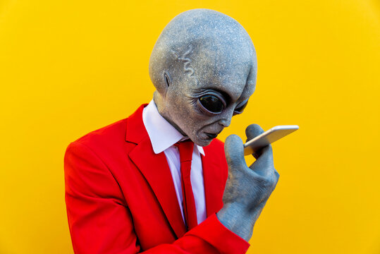 Portrait of man wearing alien costume and bright red suit using smart phone