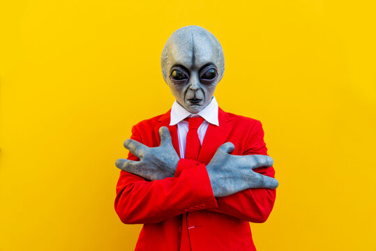 Portrait of man wearing alien costume and bright red suit standing with crossed arms