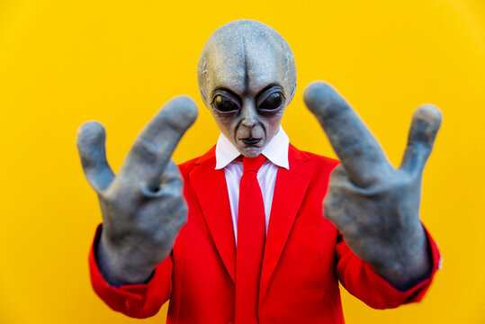 Portrait of man wearing alien costume and bright red suit showing two middle fingers