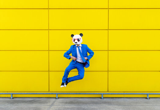 Man wearing vibrant blue suit and panda mask jumping against yellow wall