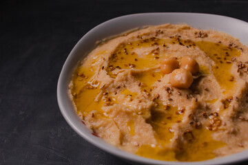 Chickpeas hummus with olive oil and toasted sesame on dark background and selective focus. 