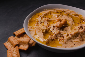 Chickpeas hummus with olive oil and toasted sesame on dark background and selective focus. 