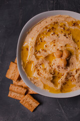 Chickpeas hummus with olive oil and toasted sesame on dark background and selective focus. 