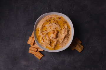 Chickpeas hummus with olive oil and toasted sesame on dark background and selective focus. 