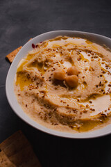 Chickpeas hummus with olive oil and toasted sesame on dark background and selective focus. 