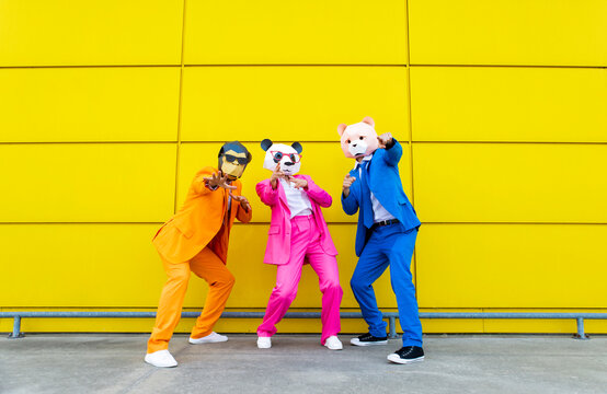 Three adults wearing vibrant suits and animal masks posing together in front of yellow wall