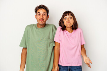 Young mixed race couple isolated on white background shrugs shoulders and open eyes confused.