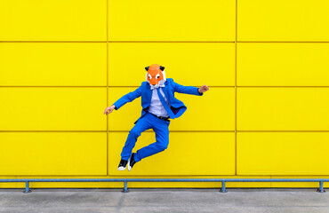 Man wearing vibrant blue suit and tiger mask jumping against yellow wall
