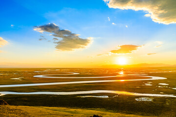 Bayinbuluke Grassland and winding river natural scenery in Xinjiang at sunset,China.The winding river is on the green grassland.